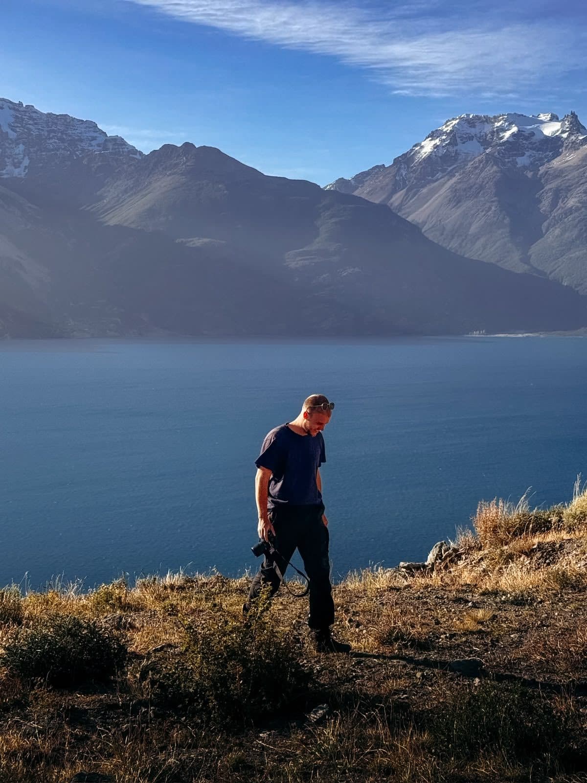 Guus Alderden walking along a ridge above a mountain lake, camera in hand